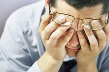 primer plano de hombre con camisa y corbata con gafas preocupado llevándose las manos a los ojos